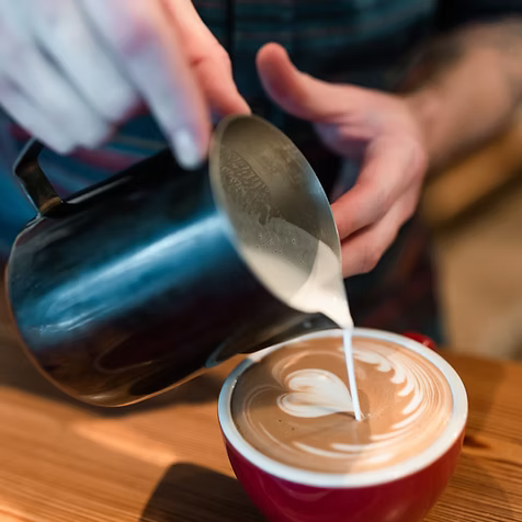 Person pouring milk into a cup of coffee to create a latte art design.